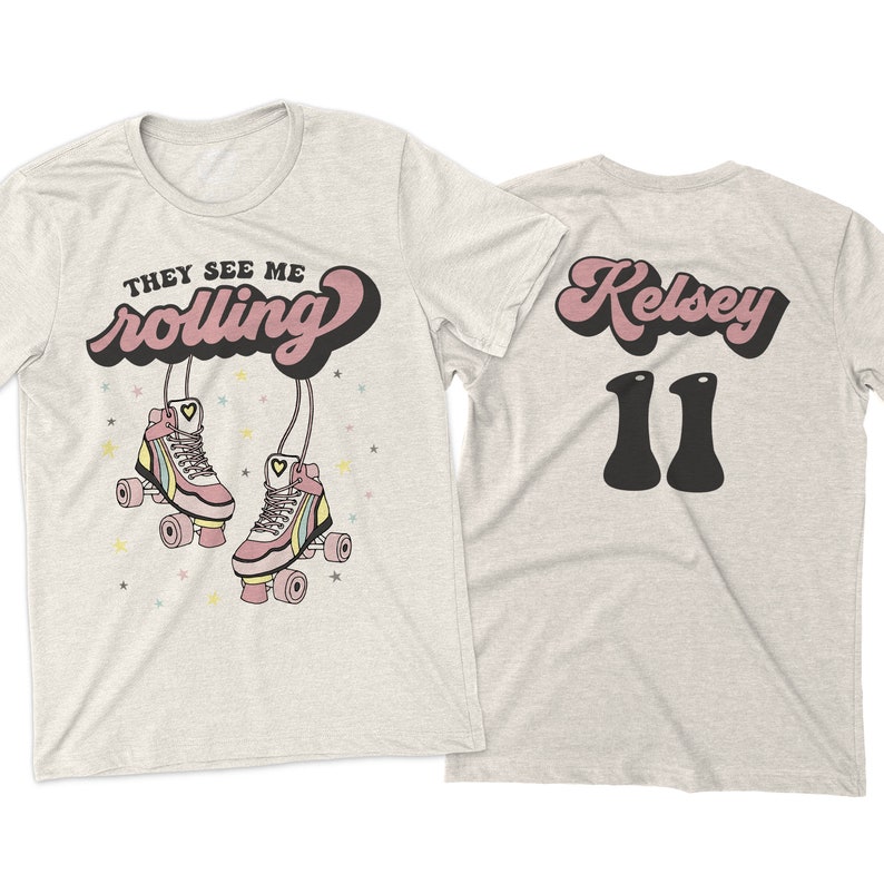 Puede incluir: Dos camisetas de color gris jaspeado. La parte delantera de una camiseta tiene el texto "They See Me Rolling" en rosa y negro con un par de patines de ruedas rosas con rayas arco&iacute;ris. La parte trasera de la otra camiseta tiene el texto "Kelsey 11" en rosa y negro.