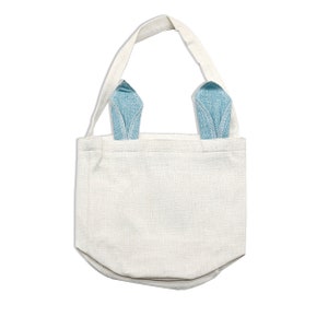 May include: A white canvas tote bag with blue denim bunny ears. The bag has a simple design and is ideal for carrying small items.