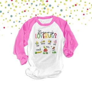 May include: A white and pink long-sleeved baseball t-shirt with the text "Grammy's Lovebugs" in rainbow letters.  The shirt features a variety of colorful bugs with names written underneath each bug: Finn, Molly, Liam, Kate, Connor, Rory, and Luke.