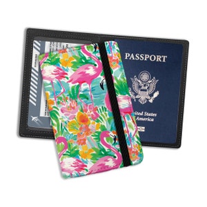May include: Black passport holder with a colorful flamingo print. The holder has a black elastic band and holds a U.S. passport and a boarding pass. The flamingo design includes pink flamingos, flowers, and a turquoise background.