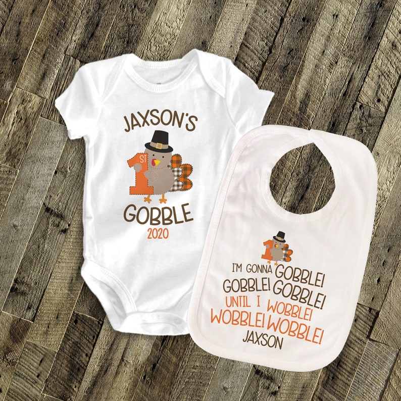 May include: White baby bodysuit and bib with a Thanksgiving turkey design. The bodysuit says "Jaxson's 1st Gobble 2020". The bib says "I'm gonna gobble gobblei gobblei until I wobblei wobblei wobblei Jaxson".