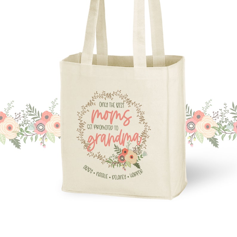 May include: A white canvas tote bag featuring a floral wreath design with the text "Only the best moms get promoted to grandma". The wreath is brown with pink flowers and green leaves. The text is in pink and brown. The names "Abby, Natalie, Delaney, Harper" are printed below the wreath.