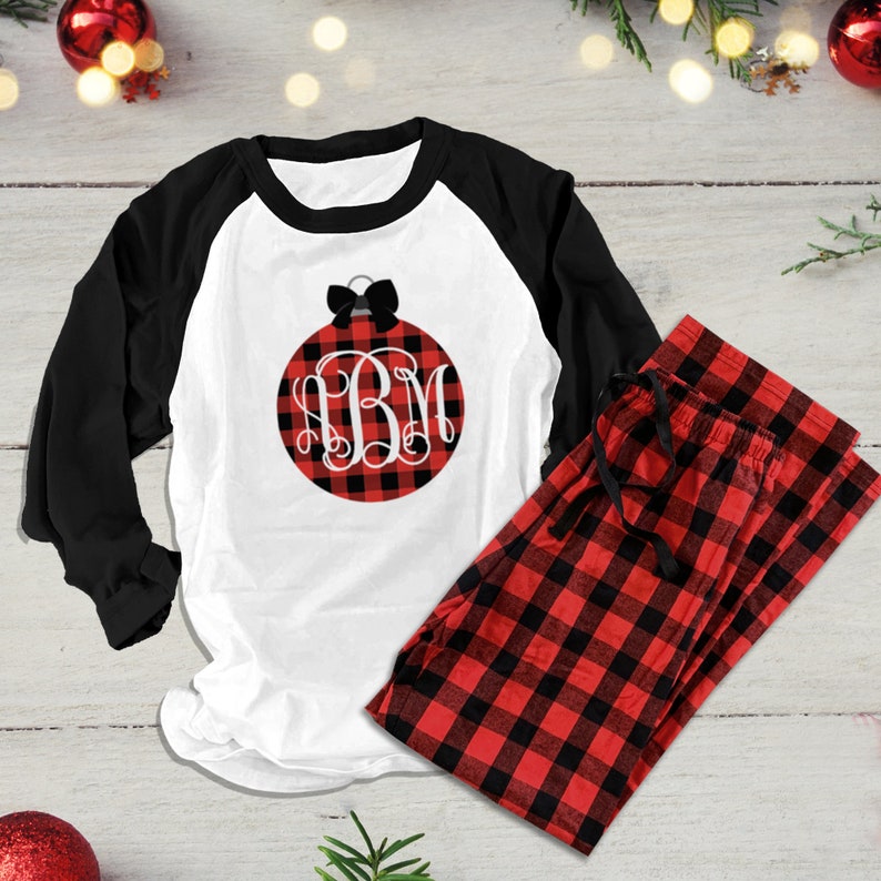 Op de afbeelding: Rode en zwarte buffalo plaid pyjamaset met een wit longsleeve shirt met een zwarte strik en een rode en zwarte buffalo plaid ornament met het monogram "BM".