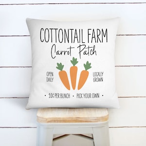 May include: White pillow with a black and white sign that says "COTTONTAIL FARM Carrot Patch". The sign also says "Open Daily", "Locally Grown", and "10¢ per bunch - Pick your own". There are three orange carrots with green tops on the sign.