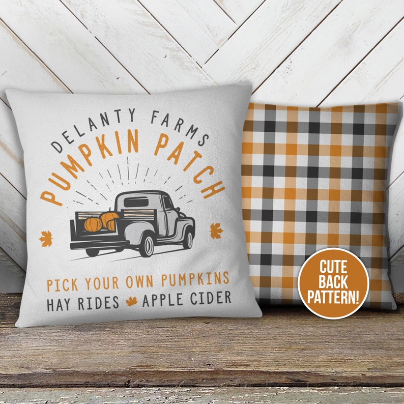 May include: A white pillow with a vintage truck design and the text "Delanty Farms Pumpkin Patch" in a circle. The text "Pick your own pumpkins, hay rides, apple cider" is below the truck. The back of the pillow is a black and orange plaid pattern with the text "Cute Back Pattern!"