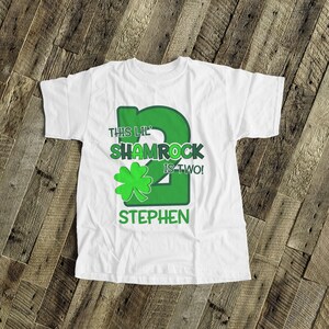 May include: White t-shirt with a green shamrock and the text "This Lil' Shamrock is Two!" and a personalized name "Stephen".