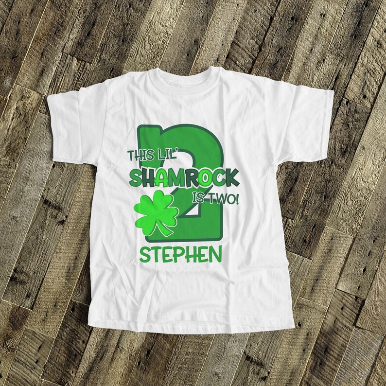 May include: White t-shirt with a green shamrock and the text "This Lil' Shamrock is Two!" and a personalized name "Stephen".