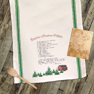 May include: A white kitchen towel with green stripes and a red barn illustration. The towel features a handwritten recipe for "Grandma's Christmas Potatoes" with ingredients including potatoes, cheddar cheese, sour cream, and green peppers.