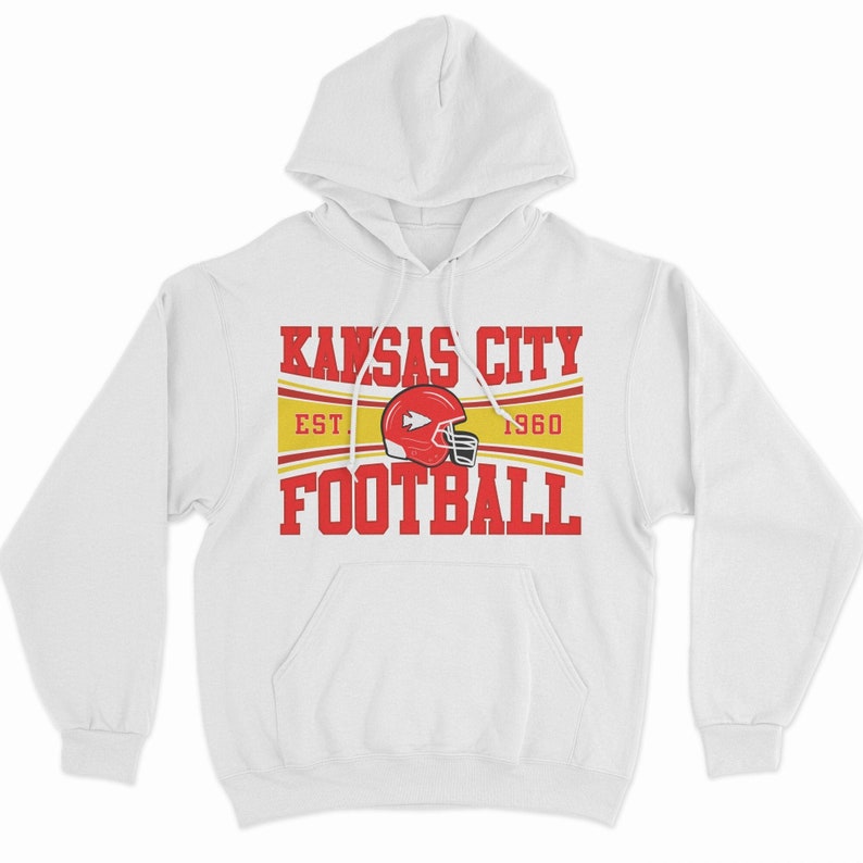 May include: White hooded sweatshirt with a red and yellow graphic that says "Kansas City Football" with the team logo and "Est. 1960" underneath.