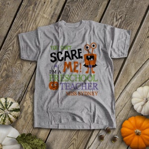 May include: Gray t-shirt with a Halloween-themed design. It says "You can't scare me! I'm a preschool teacher Miss Sydney" with a cartoon monster and a pumpkin.