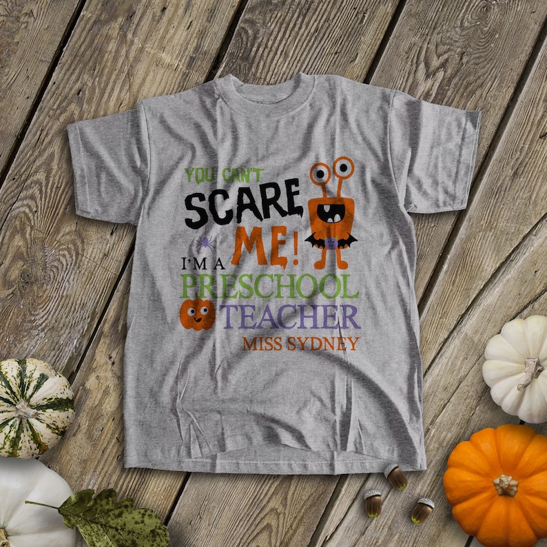May include: Gray t-shirt with a Halloween-themed design. It says "You can't scare me! I'm a preschool teacher Miss Sydney" with a cartoon monster and a pumpkin.
