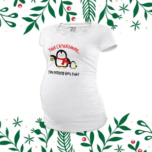 May include: White maternity t-shirt featuring a penguin graphic and the text "This Christmas... I'm eating for two!"