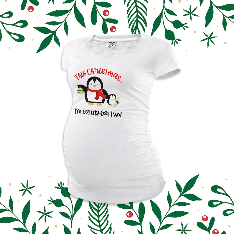 May include: White maternity t-shirt featuring a penguin graphic and the text "This Christmas... I'm eating for two!"
