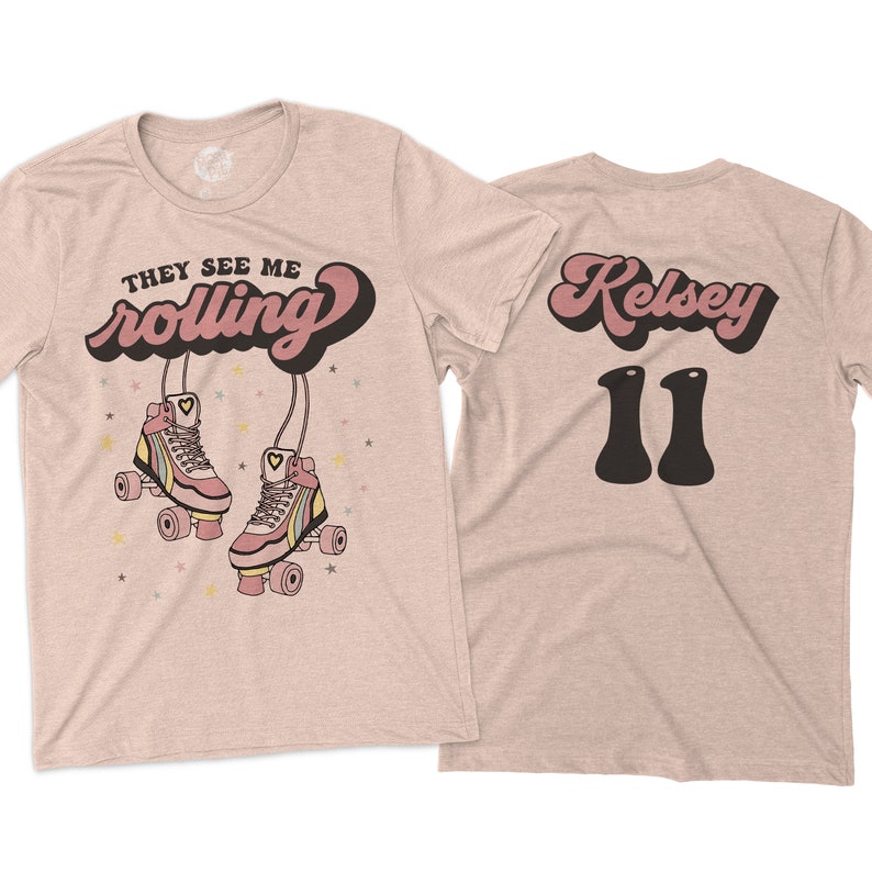 Puede incluir: Una camiseta rosa claro con el texto "They See Me Rolling" en una fuente retro con un coraz&oacute;n en la palabra "rolling". La camiseta presenta un par de patines rosas con rayas arco&iacute;ris y un coraz&oacute;n en cada pat&iacute;n. La parte posterior de la camiseta tiene el texto "Kelsey 11" en una fuente retro.