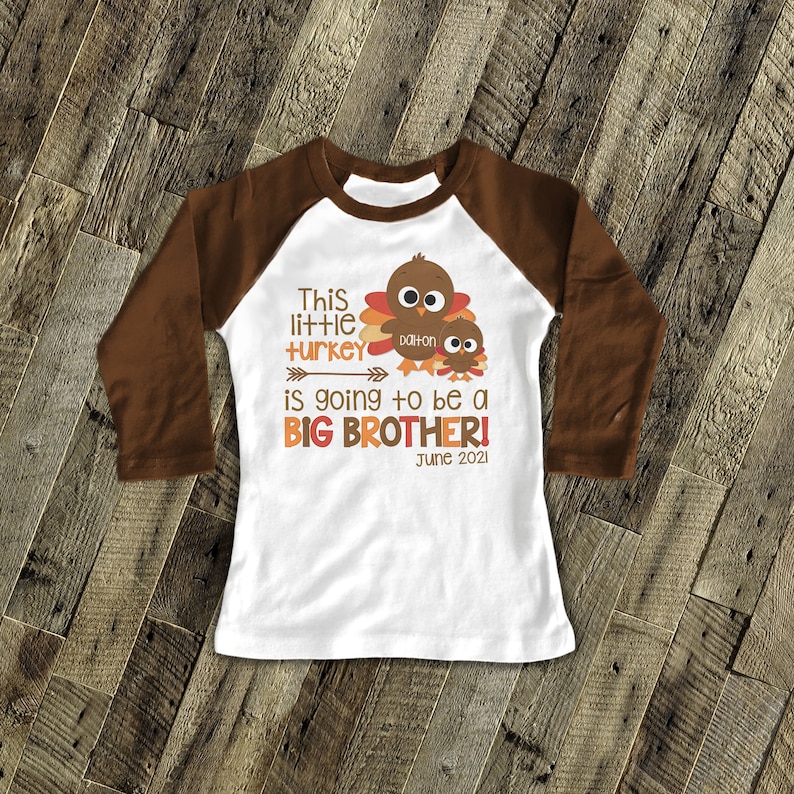 K&ouml;nnte beinhalten: Ein wei&szlig;es Langarmshirt mit braunen &Auml;rmeln. Das Shirt zeigt eine Truthahn-Grafik mit dem Text "This little turkey is going to be a BIG BROTHER! June 2021" und dem Namen "Dalton".