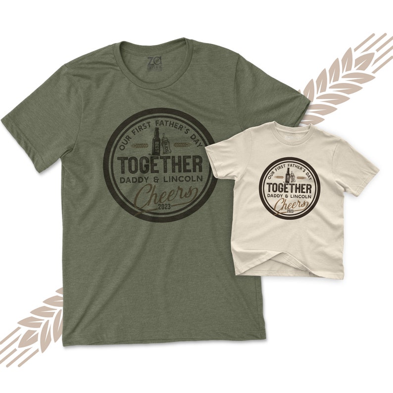 May include: Two green and beige t-shirts with a brown circle graphic that says "Our First Father's Day Together Daddy & Lincoln Cheers 2023".