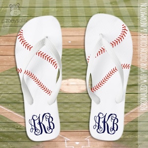 May include: A pair of white flip flops with a baseball stitch design and a navy blue monogram "AKB" on each. The flip flops are on a wooden surface with a baseball field design.
