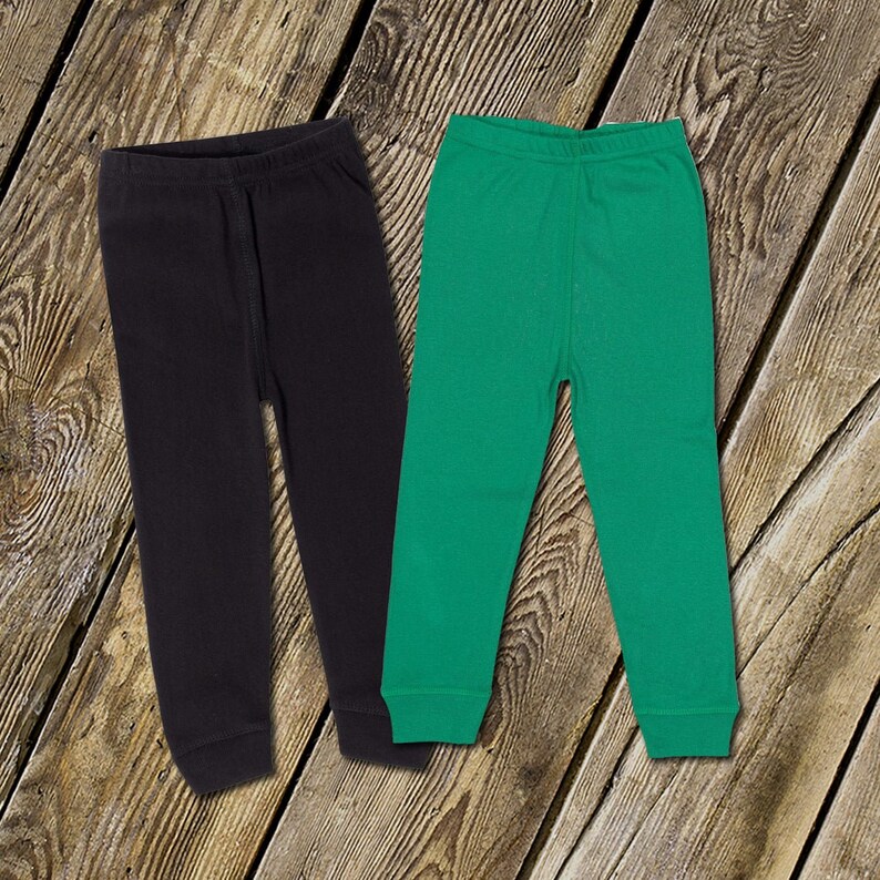 Op de afbeelding: Twee paar effen leggings, een zwarte en een groene, op een houten oppervlak gelegd.