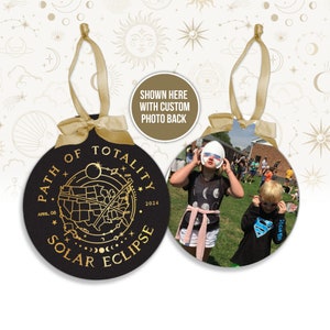 May include: Black round ornament with gold text and a photo back. The front reads "PATH OF TOTALITY SOLAR ECLIPSE APRIL, 08 2024" with a map of the U.S. and celestial designs. A gold ribbon is attached for hanging.