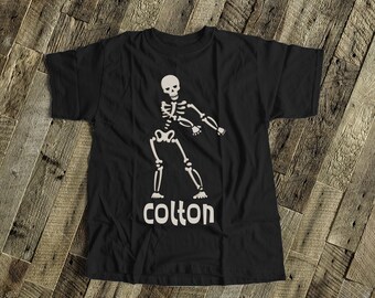 May include: Black t-shirt with a white skeleton dancing and the name "Colton" printed below.