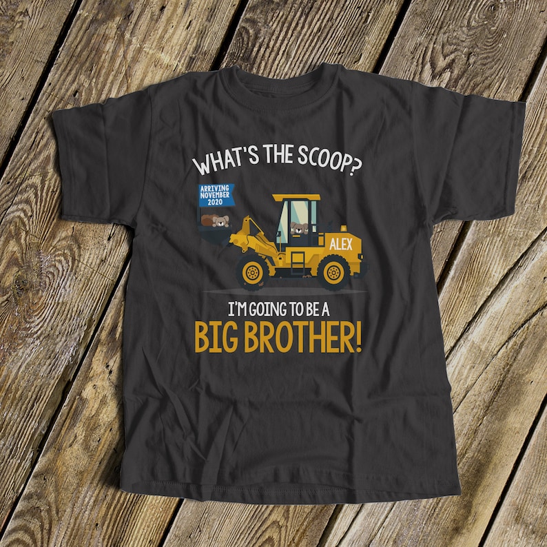 Puede incluir: Camiseta gris oscuro con el texto "WHAT'S THE SCOOP? I'M GOING TO BE A BIG BROTHER!" y un gr&aacute;fico de una cargadora frontal amarilla. La cargadora tiene el nombre "ALEX" y un letrero que dice "ARRIVING NOVEMBER 2020".