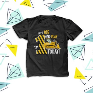 May include: Black t-shirt featuring a yellow and black striped number 1 and a bulldozer graphic. The text on the shirt reads "Let's Dig and Play, I'm 1 Today!" and includes a name. This is a birthday-themed garment.