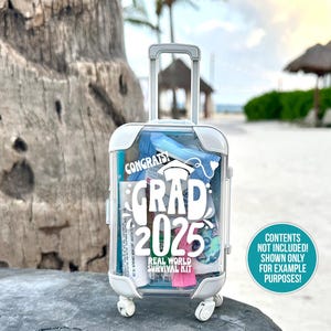 May include: A white plastic suitcase with a clear front, decorated with a white sticker that says "Congrats! Grad 2025 Real World Survival Kit". The suitcase has a handle and wheels.