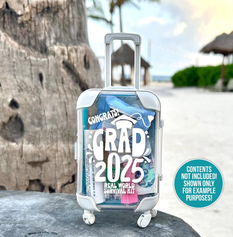 May include: A white plastic suitcase with a clear front, decorated with a white sticker that says "Congrats! Grad 2025 Real World Survival Kit". The suitcase has a handle and wheels.