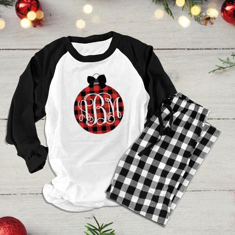 Op de afbeelding: Witte en zwarte geruite pyjamaset met een shirt met lange mouwen met een rood en zwart buffalo plaid ornament met een zwarte strik en een wit monogram "BM".