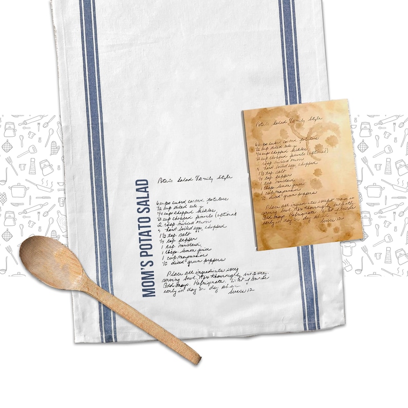 May include: A white kitchen towel with blue stripes and a handwritten recipe for "Mom's Potato Salad" in black ink. The recipe includes ingredients like celery, potatoes, and mayonnaise. The towel is decorated with a pattern of kitchen utensils.