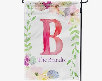 Peut inclure: Un drapeau de jardin blanc avec une lettre B rose en aquarelle entourée d'une couronne de feuilles vertes, de fleurs en aquarelle et d'œufs tachetés. Le texte "The Brandts" est écrit en violet sous la lettre.