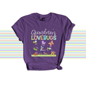 May include: A purple short-sleeve t-shirt featuring the white and multicolored text Grandma's LOVEBUGS. Below the text are illustrations of various insects including bees, butterflies, a dragonfly, a ladybug, and a caterpillar, each with a name.