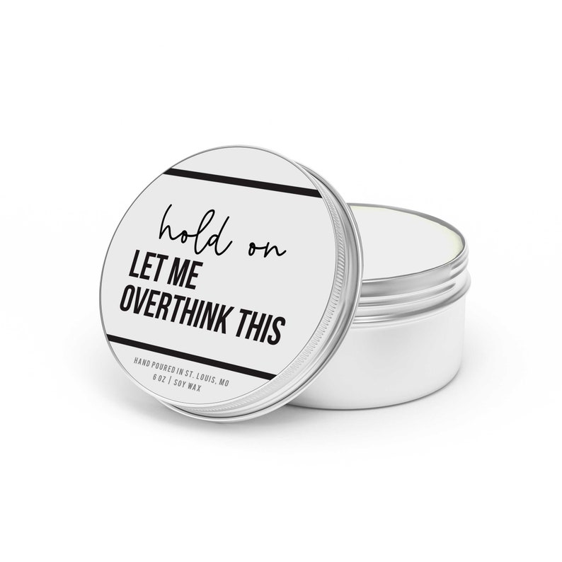 May include: A silver candle tin with a white label that reads "hold on LET ME OVERTHINK THIS" and "HAND POURED IN ST. LOUIS, MO 6 OZ | SOY WAX".