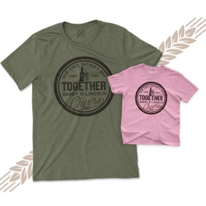 May include: Two t-shirts, one green and one pink, with a brown circle graphic that says "Our First Father's Day Together Daddy & Lincoln Cheers 2023".