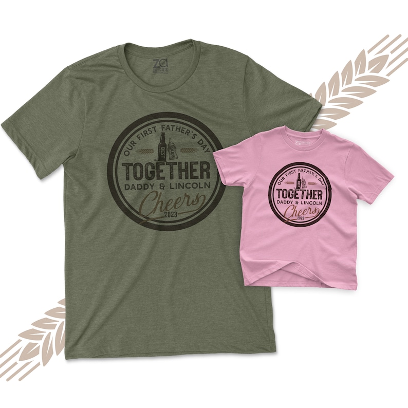 May include: Two t-shirts, one green and one pink, with a brown circle graphic that says "Our First Father's Day Together Daddy & Lincoln Cheers 2023".