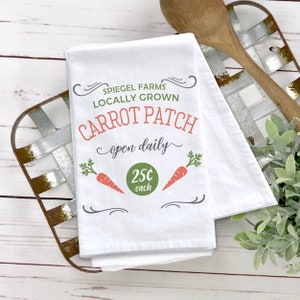 May include: White kitchen towel with a green and red design. The text on the towel reads "Spiegel Farms Locally Grown Carrot Patch open daily 25c each".