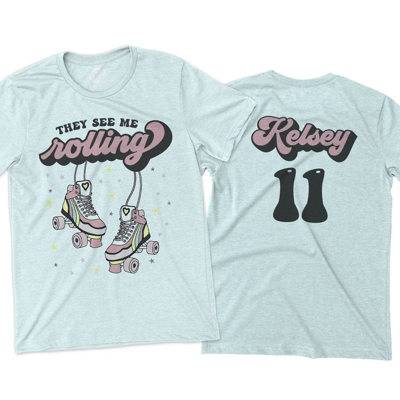 Puede incluir: Camiseta azul claro con el texto "They See Me Rolling" en una fuente retro con patines y estrellas. La parte posterior de la camiseta tiene el nombre "Kelsey" en una fuente retro y el n&uacute;mero "11" en negro.