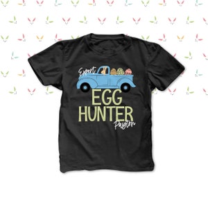 May include: Black t-shirt featuring a light blue truck graphic with Easter eggs. The text on the shirt reads "Expert Egg Hunter Payton". The design includes a bunny in the truck and a bunny ears pattern.