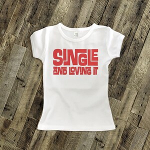 May include: White t-shirt with red text that reads "SINGLE AND LOVING IT".