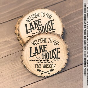 May include: Two wooden round slices with the text "Welcome to our Lake House" and "The Wilsons" with a graphic of two crossed oars.
