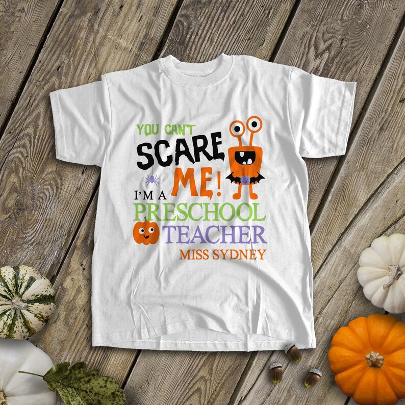 May include: White t-shirt with a Halloween-themed design. It features a cartoon monster with the text "You can't scare me! I'm a preschool teacher Miss Sydney".
