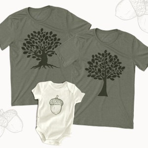 May include: A set of three shirts featuring an oak tree design. The adult shirts are green with a black oak tree design. The baby shirt is white with a black acorn design.
