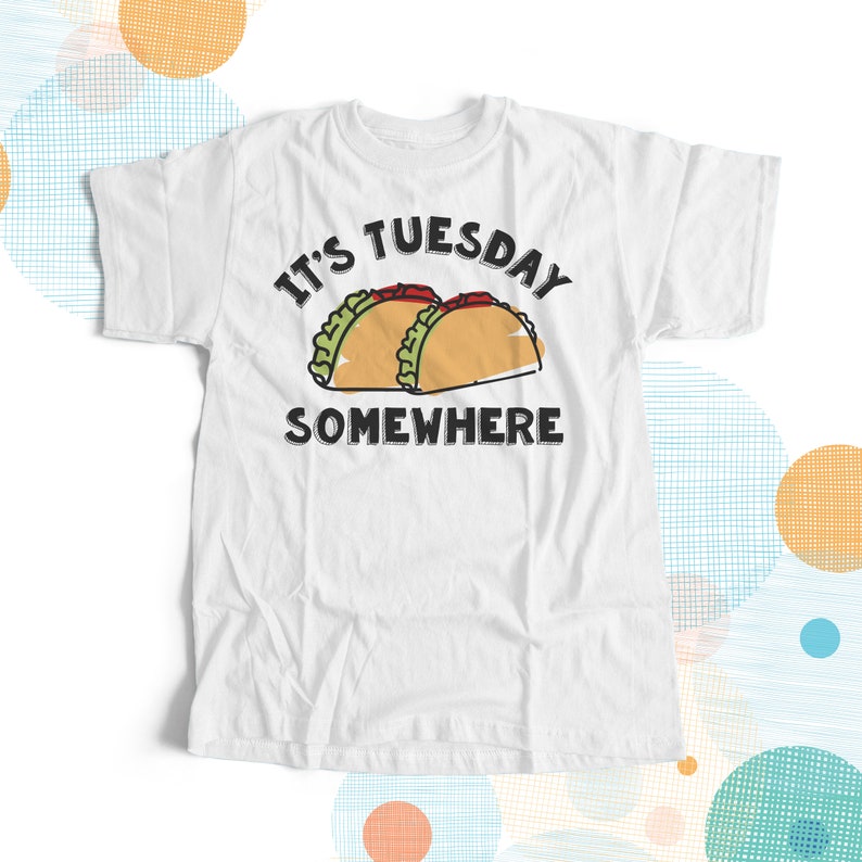 May include: White t-shirt with black text that reads "It's Tuesday Somewhere" and a cartoon image of two tacos.