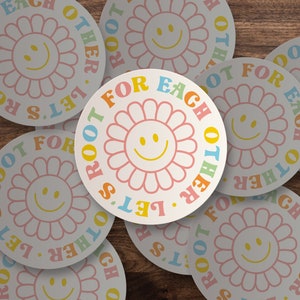 May include: A set of colorful round stickers with a flower and smiley face design. The stickers feature the text "Let's Root For Each Other".
