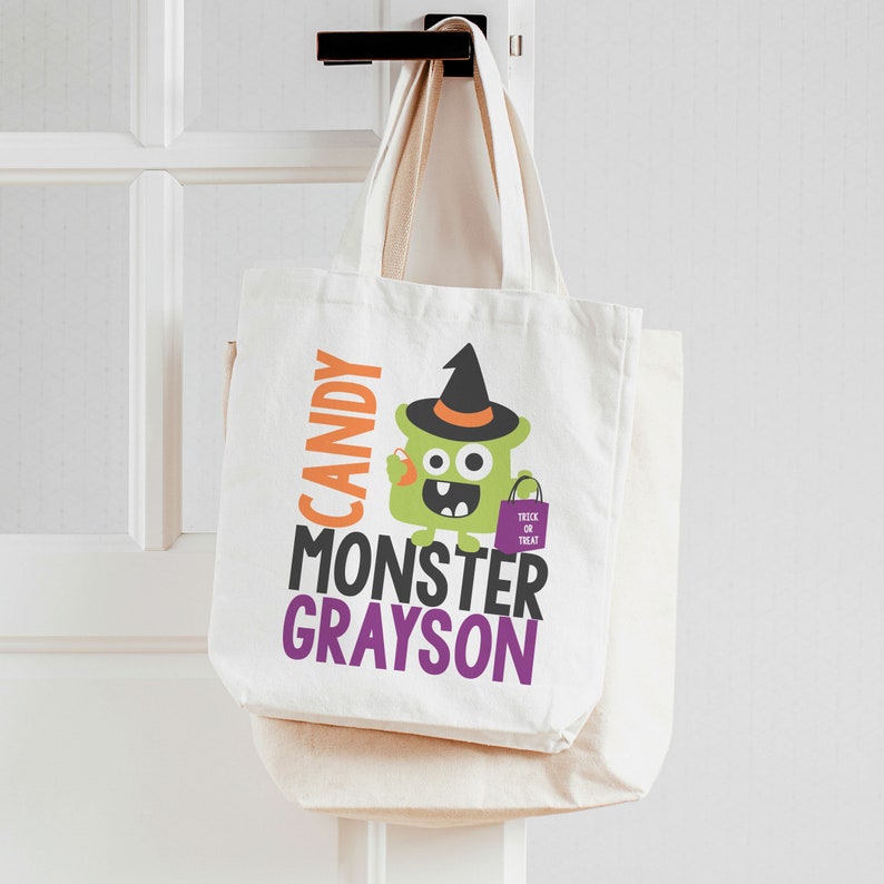 Puede incluir: Bolsa de lona blanca con un monstruo verde que lleva un sombrero de bruja y sostiene una bolsa morada de truco o trato. El texto en la bolsa dice "Candy Monster Grayson".