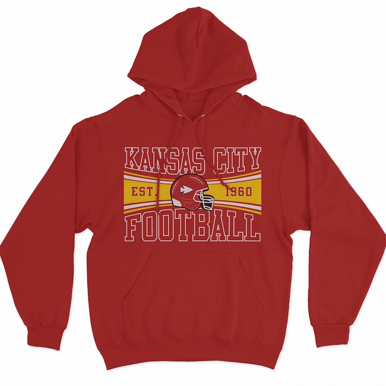 May include: Red hooded sweatshirt with a white graphic design that says "Kansas City Football" with a yellow stripe and the text "Est. 1960" underneath. The graphic also includes a red football helmet with a white arrow.