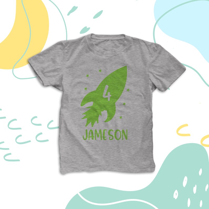 K&ouml;nnte beinhalten: Ein graues T-Shirt mit einem gr&uuml;nen Raketen-Design und der Zahl 4 in der Rakete. Der Text "JAMESON" befindet sich unter der Rakete.