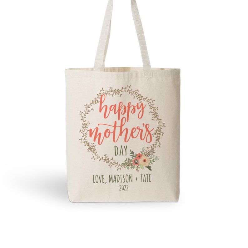 May include: A beige canvas tote bag with a floral wreath design and the text "happy mother's day" in coral. The bag also includes the text "Love, Madison + Tate 2022".
