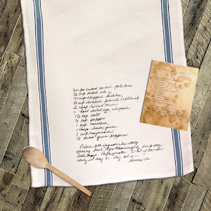 May include: A handwritten recipe for a salad on a white kitchen towel with blue stripes. The recipe includes ingredients like diced celery, chopped pickles, chopped tomato, boiled eggs, salt, pepper, mustard, lemon juice, mayonnaise, and green peppers. The recipe also includes instructions for preparing the salad, such as placing all ingredients in a serving bowl, mixing thoroughly, and refrigerating.