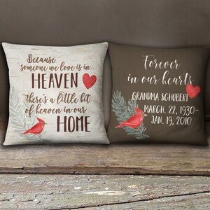May include: Two decorative throw pillows with a brown background and a white background. The white pillow has a red heart and the text "Because someone we love is in HEAVEN there's a little bit of heaven in our HOME". The brown pillow has a red heart and the text "Forever in our hearts GRANDMA SCHUBERT MARCH. 22, 1930- JAN. 19, 2010".
